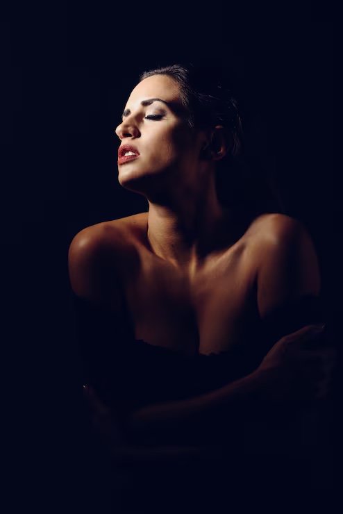 Mulher de olhos fechados, em luz suave sobre fundo escuro.